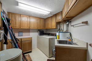 Washroom with cabinets, a textured ceiling, sink, water heater, and washing machine and dryer