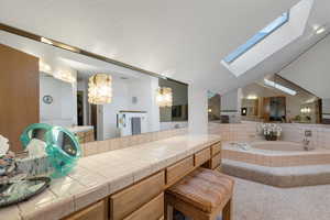 Bathroom with vanity, tiled tub, and vaulted ceiling with skylight