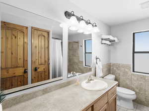 Bathroom with vanity, a healthy amount of sunlight, toilet, and tile walls