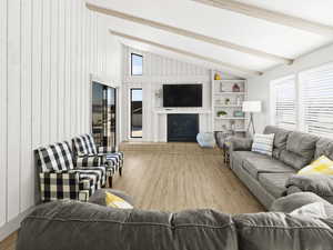 Living room featuring lofted ceiling with beams, wooden walls, light wood-type flooring, and a brick fireplace