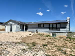 View of front of property featuring an attached garage, a chimney, metal roof, and driveway