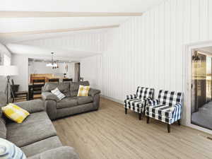 Living room with sink, vaulted ceiling with beams, a notable chandelier, wooden walls, and light wood-type flooring