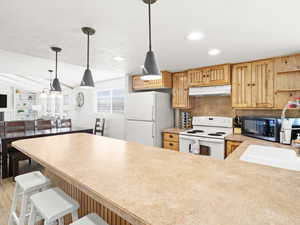 Kitchen with white appliances, backsplash, a kitchen breakfast bar, vaulted ceiling, and kitchen peninsula