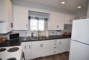 Kitchen with white cabinets, dark wood-type flooring, sink, and white appliances