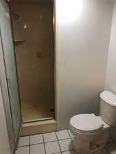 Bathroom featuring tile patterned flooring, toilet, and a shower with door