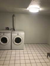 Laundry area with light tile patterned floors, washer and dryer, and a textured ceiling