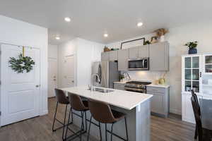 Kitchen with appliances with stainless steel finishes, a center island with sink, gray cabinets, dark hardwood / wood-style floors, and a breakfast bar area