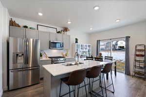 Kitchen with gray cabinetry, a kitchen island with sink, sink, and appliances with stainless steel finishes