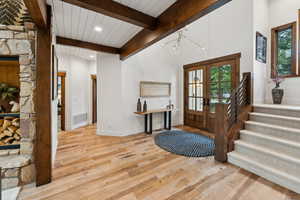 Foyer entrance with french doors, vaulted ceiling with beams, light hardwood / wood-style floors, and a wealth of natural light