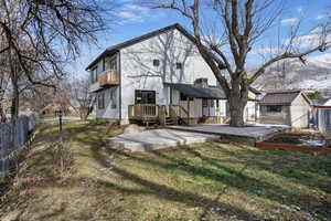 Back of house with a mountain view, a balcony, a storage unit, and a lawn