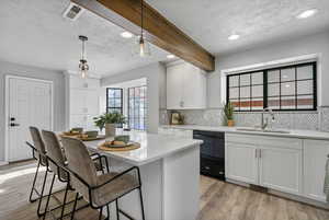 Kitchen with pendant lighting, dishwasher, white cabinets, sink, and beamed ceiling