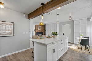 Kitchen with white cabinets, light wood-type flooring, a kitchen island, and beamed ceiling