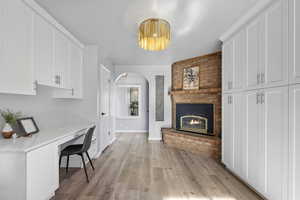 Home office with built in desk, light hardwood / wood-style floors, and a brick fireplace