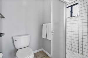 Bathroom with hardwood / wood-style floors, toilet, and a tile shower