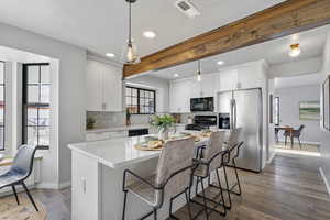 Kitchen with a center island, black appliances, beamed ceiling, decorative light fixtures, and white cabinetry