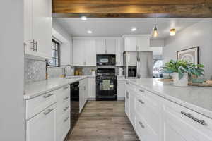 Kitchen with black appliances, light stone counters, white cabinetry, and sink