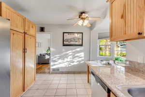 Kitchen with light brown cabinetry, stainless steel dishwasher, ceiling fan, and light tile patterned flooring