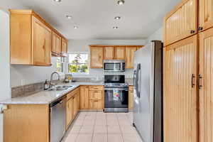 Kitchen with light brown cabinetry, light stone counters, stainless steel appliances, sink, and light tile patterned floors