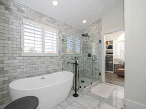 Primary Bathroom with euro glass shower,  separate freestanding tub, plenty of natural light, lofted ceiling, and custom tile