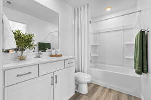 Full bathroom with wood-type flooring, vanity, toilet, and shower / bath combination with curtain