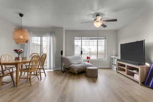 Sitting room with a textured ceiling, light hardwood / wood-style floors, ceiling fan, and a healthy amount of sunlight