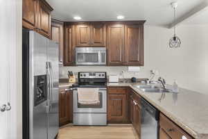 Kitchen featuring sink, hanging light fixtures, light hardwood / wood-style flooring, a textured ceiling, and appliances with stainless steel finishes