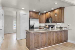 Kitchen featuring kitchen peninsula, a textured ceiling, stainless steel appliances, decorative light fixtures, and light hardwood / wood-style floors