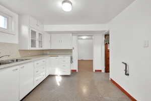 Kitchen with backsplash, white cabinetry, and sink