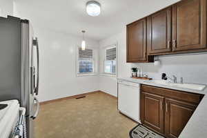 Kitchen featuring stainless steel fridge, stove, white dishwasher, sink, and hanging light fixtures