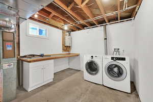 Washroom featuring cabinets, tankless water heater, and washing machine and dryer