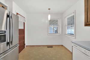 Kitchen featuring stainless steel fridge, white dishwasher, and hanging light fixtures