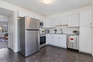 Kitchen with backsplash, sink, light stone counters, white cabinetry, and stainless steel appliances