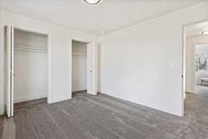 Unfurnished bedroom with multiple closets, crown molding, and carpet floors