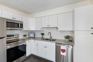 Kitchen featuring light stone countertops, appliances with stainless steel finishes, white cabinetry, and sink