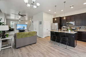 Kitchen with ceiling fan with notable chandelier, hanging light fixtures, dark brown cabinets, a center island with sink, and appliances with stainless steel finishes