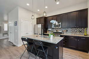 Kitchen with a kitchen island with sink, hanging light fixtures, light hardwood / wood-style floors, light stone counters, and stainless steel appliances