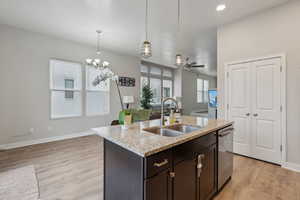 Kitchen with dishwasher, sink, light stone counters, an island with sink, and ceiling fan with notable chandelier