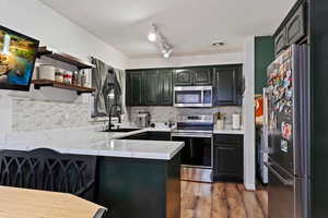 Kitchen with kitchen peninsula, appliances with stainless steel finishes, decorative backsplash, and sink