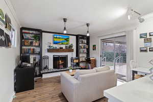 Living room with wood-type flooring, track lighting, and a brick fireplace