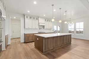 Kitchen featuring gas stovetop, plenty of natural light, pendant lighting, a center island with sink, and white cabinets