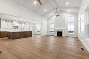 Unfurnished living room featuring beam ceiling, a brick fireplace, light hardwood / wood-style flooring, high vaulted ceiling, and ceiling fan with notable chandelier