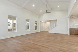 Unfurnished living room featuring ceiling fan, beam ceiling, light hardwood / wood-style floors, and high vaulted ceiling