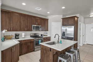 Kitchen featuring sink, light tile patterned floors, stainless steel appliances, and a kitchen island with sink