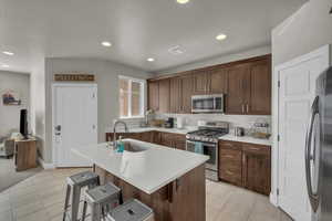 Kitchen featuring sink, an island with sink, a breakfast bar, light tile patterned floors, and appliances with stainless steel finishes