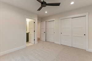 Unfurnished bedroom featuring ceiling fan, light carpet, connected bathroom, and two closets