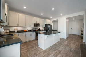 Kitchen featuring stainless steel appliances, sink, wood-type flooring, white cabinetry, and a kitchen island