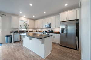 Kitchen with a breakfast bar, a center island, light hardwood / wood-style floors, white cabinetry, and stainless steel appliances