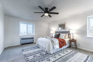 Bedroom with radiator heating unit, carpet floors, ceiling fan, and crown molding