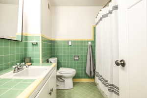 Bathroom featuring tile patterned flooring, vanity, toilet, and tile walls