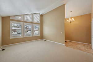 Living room view from the dining area featuring light colored carpet, lofted ceiling, and an inviting chandelier